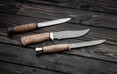 Hunting bowie knife with a wooden handle on dark wooden background. Steel arms weapon. top view