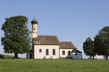 Fototapeta na wymiar die einsame Kirche St. Johannes der Täufer steht vor den Satellitenkommunikationsanlagen in Raisting , Oberbayern