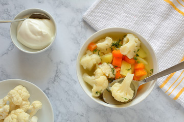Cauliflower soup with fresh vegetables in a bowl.