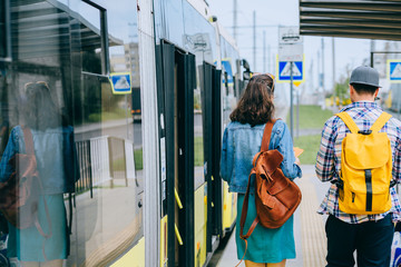 Young couple, hipster man and woman students traveler with backpacks on tram stop going along...