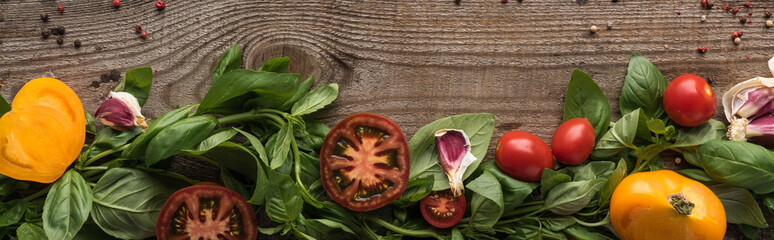 panoramic shot of spinach, sliced tomatoes, garlic and scattered pepper on wooden table