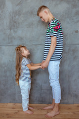 stylish caucasian siblings (brother and sister) in striped t-shirts and white pants standing in loft interior. Family, fashion, relatives, relationship and children concept.