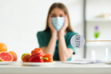 selective focus of woman in medical mask propping face with hands and nameplate with inscription...