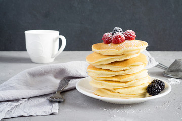 American pancakes with raspberries, blackberries and powdered sugar for breakfast on a gray concrete background with copy space