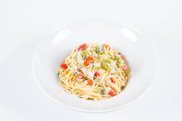 Spaghetti with cream sauce with smoked mackerel, peas ,bell pepper and some parsley on a white plate on a white background