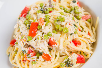 Spaghetti with cream sauce with smoked mackerel, peas ,bell pepper and some parsley on a white plate on a white background