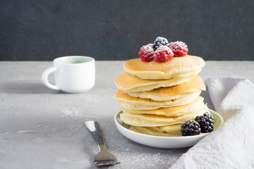 American pancakes with raspberries, blackberries and powdered sugar for breakfast on a gray concrete background with copy space