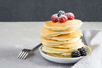 American pancakes with raspberries, blackberries and powdered sugar for breakfast on a gray concrete background with copy space