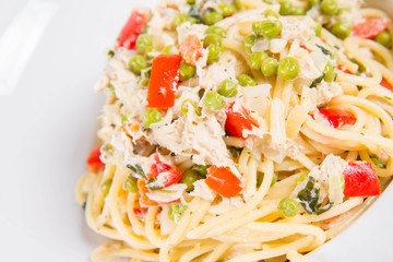 Spaghetti with cream sauce with smoked mackerel, peas ,bell pepper and some parsley on a white plate on a white background