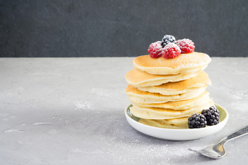 American pancakes with raspberries, blackberries and powdered sugar for breakfast on a gray concrete background with copy space