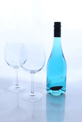 Wine bottle with blue wine next to two wine glasses against a white  background with reflection of the glass. 