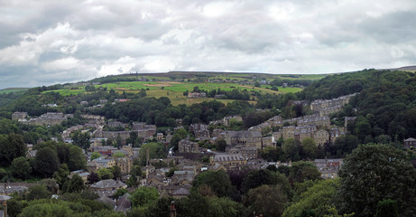 Obraz premium a wide panoramic view of the town of hebden bridge with hillside streets surrounded by trees and pennine fields