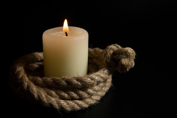 Fototapeta na wymiar Coiled rope with burning candle on dark background