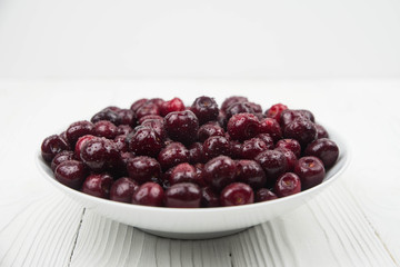 A lot of fresh sweet cherry fruit berries with water drops, close up on the plate on white background. Close up of pile of ripe cherries. Large collection of fresh red cherries. Ripe cherries texture 