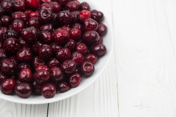 A lot of fresh sweet cherry fruit berries with water drops, close up on the plate on white background. Close up of pile of ripe cherries. Large collection of fresh red cherries. Ripe cherries texture 