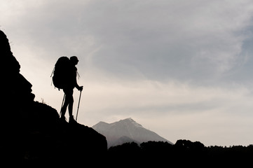 Silhouette girl standing on the rocks with hiking backpack and walking sticks