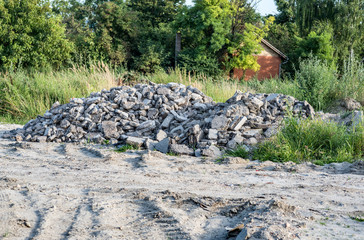 Big pile of tarmac or asphalt road parts cracked and demolished dumped on the sandy field after replacement of old street selective focus