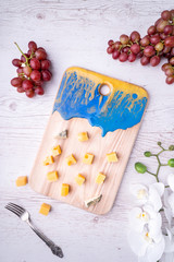 Cutting board with an abstract pattern, cheeses, honey grapes, flowers, a knife and a fork.