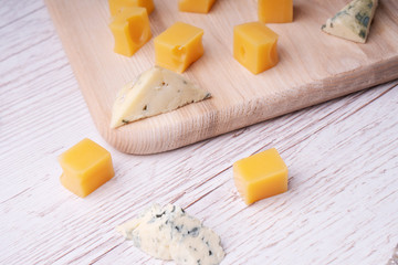 Pieces of cheddar cheese and blue roquefort on a cutting board.