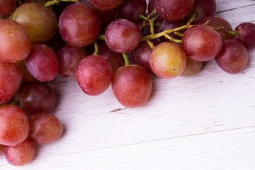A bunch of pink grapes on a wooden light tabletop.