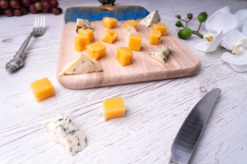 Cutting board with an abstract pattern, cheeses, honey grapes, flowers, a knife and a fork.