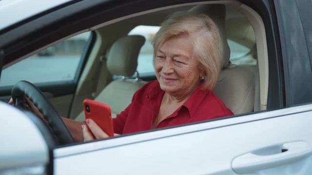 Close up senior woman sits in car uses red cell phone smile happy businesswoman blonde people smartphone cellphone communication internet search lady mobile bench browse network online slow motion