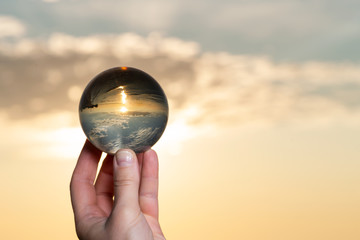 Woman's hand holding high grade Clear Quartz Sphere at the sunrise in front of the lake.