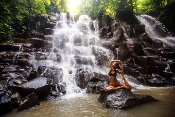 Woman practices yoga near waterfall in Bali, Indonesia