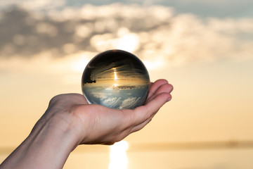 Woman's hand holding high grade Clear Quartz Sphere at the sunrise in front of the lake.