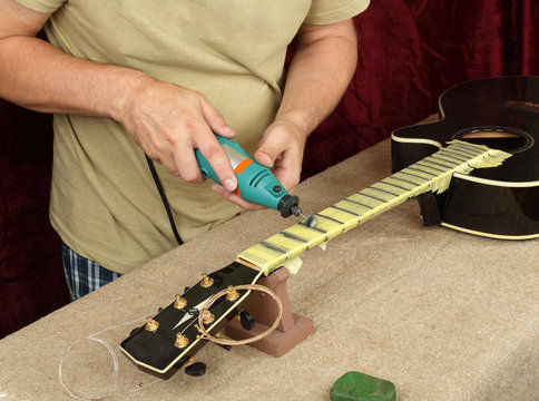 Guitar repair and service - Worker polishing acoustic guitar neck frets dremel and paste GOI