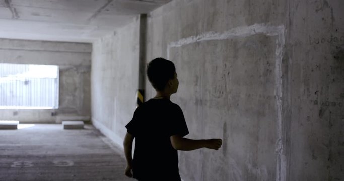Teenager kid boy soccer player using chalk to draw goals and targets on a wall in empty abandoned covered parking. 4K UHD 60 FPS RAW graded footage