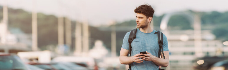 panoramic shot of handsome man in t-shirt holding smartphone and looking away