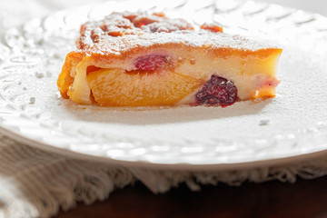 A slice of clafoutis pie with peaches, raspberries and blackberries.