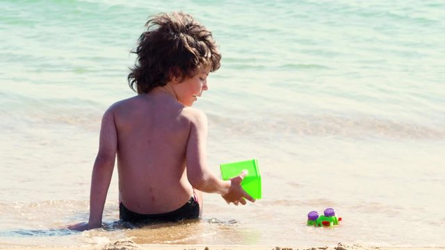 4K Back view of a young boy playing happy at the beach after the end of school. Child waiting waves on the seashore.