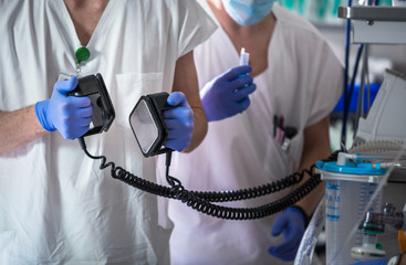 Doctor holding defibrillator electrods, performing defibrillation on a patient, saving a human life