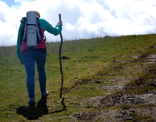 kobieta idąca po górach z plecakiem i kijem w ręku
