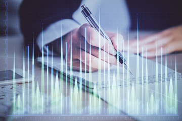 A woman hands writing information about stock market in notepad. Forex chart holograms in front....