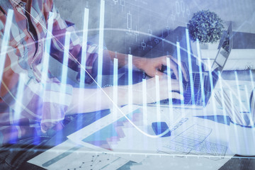 Double exposure of stock graph with businessman typing on computer in office on background. Concept of hard work.