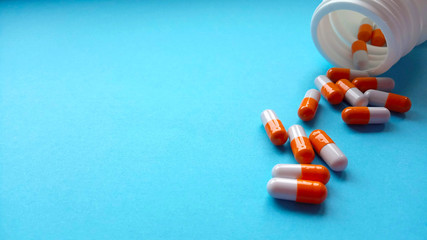 Two-color medical capsules spilled out of a bottle of medicine. Red and white pills are poured out of a jar on a blue background with copy space