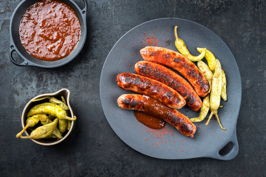 Traditional barbecue German Bratwurst with hot sauce and peperoni as top view on a modern design cast iron plate