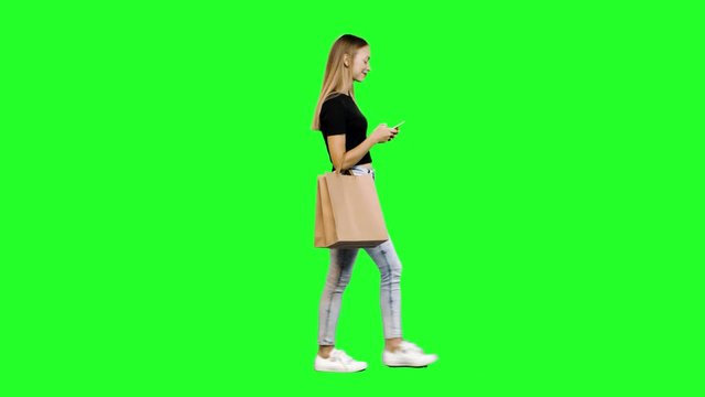 Taking a Selfie or using an app while walking, a casual young woman with shopping bags over green screen.