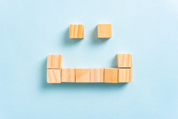 Top view of happy face concept made with wooden block squares, on paper blue background. Customer service and content marketing concept.