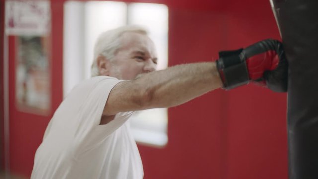 Senior man boxing combat bag at cardio training in healthy club.