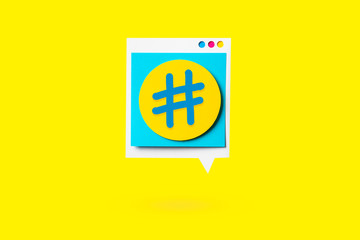Isolated paper cutout of hashtag symbol on a yellow speech bubble on yellow background. Concept of social media and digital marketing.