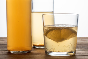 Two bottles and glass of kombucha drink on a wooden table with lemon. Soft focus.