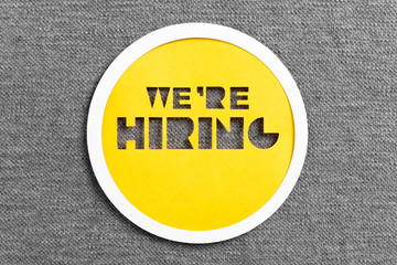 Letters cut on yellow paper with the message "We are hiring" on a gray cloth background