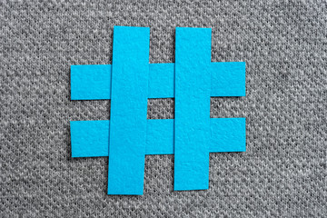 Blue hashtag symbol made with blue paper on a fabric and textured gray background