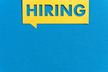 "HIRING". Yellow speech bubble banner on blank blue textured background. Job vacant and employment concept with copy space.