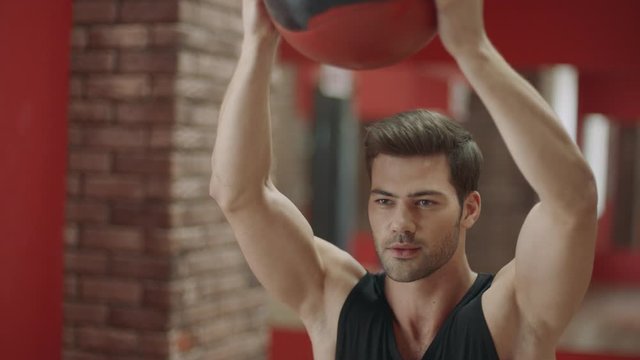 Handsome man making squat exercise with ball in fitness club.