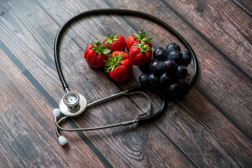Stethoscope with strawberries and black seedless grape on top of wooden table. Medical and...